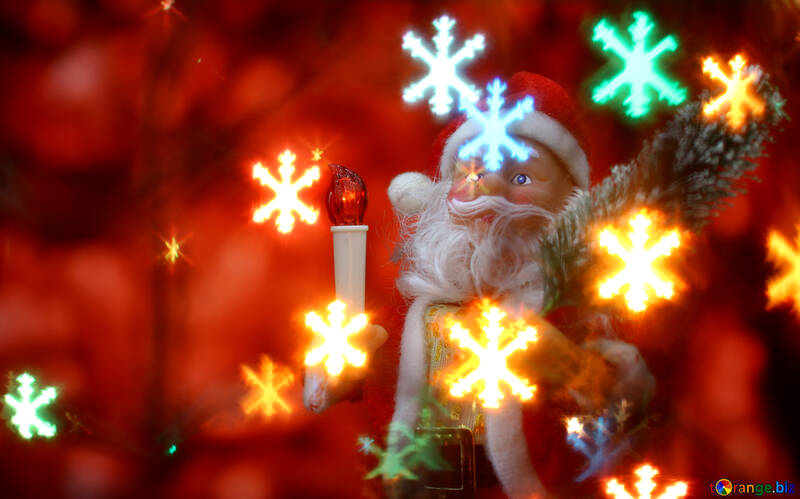 Santa Claus toy brings Christmas tree at glow red bokeh background and blurred lights snowflakes foreground.  №48174