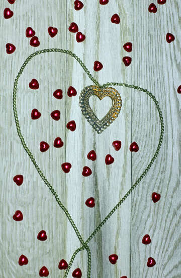 Un collier avec un pendentif coeur sur une planche de bois avec des petits coeurs rouges tout autour №49235