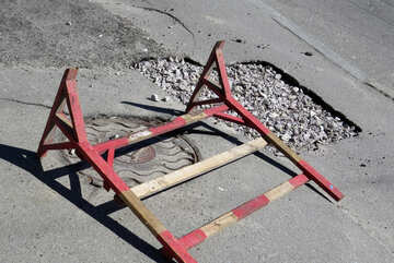 A road barrier lays on its side by a pothole №50362