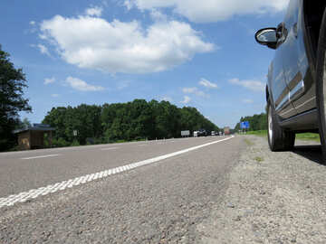 Low angle view of asphalt road, the side of a car on the right, trees at the horizon, blue sky with large cloud №52028