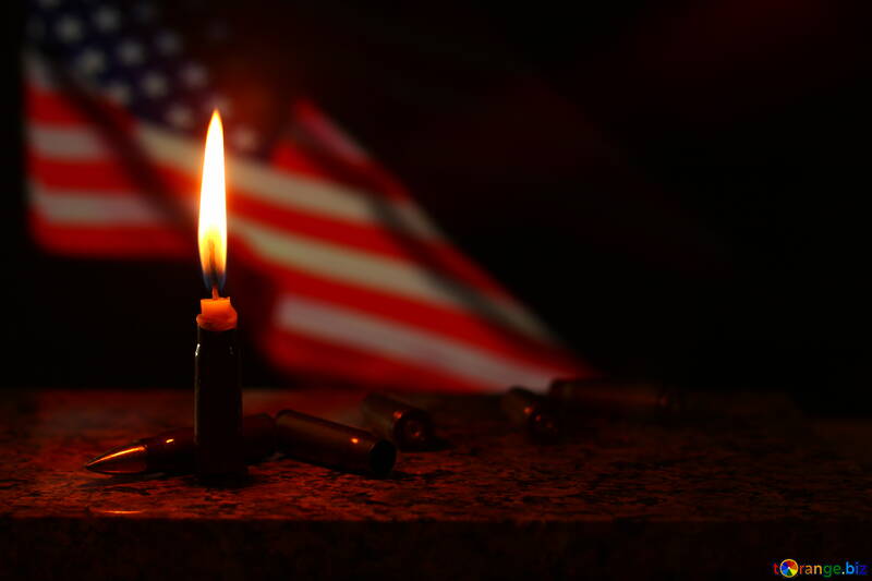 A burning candle with an American flag behind it bullets on whatever wood the candle is on United States №52527