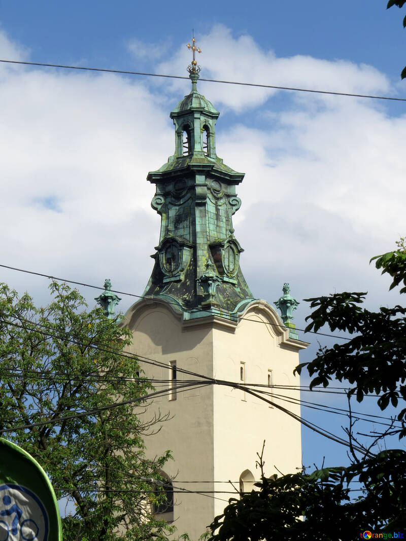 Una torre verde encima de un edificio de color mantequilla frente a un cielo azul y una blanca y esponjosa iglesia №52298