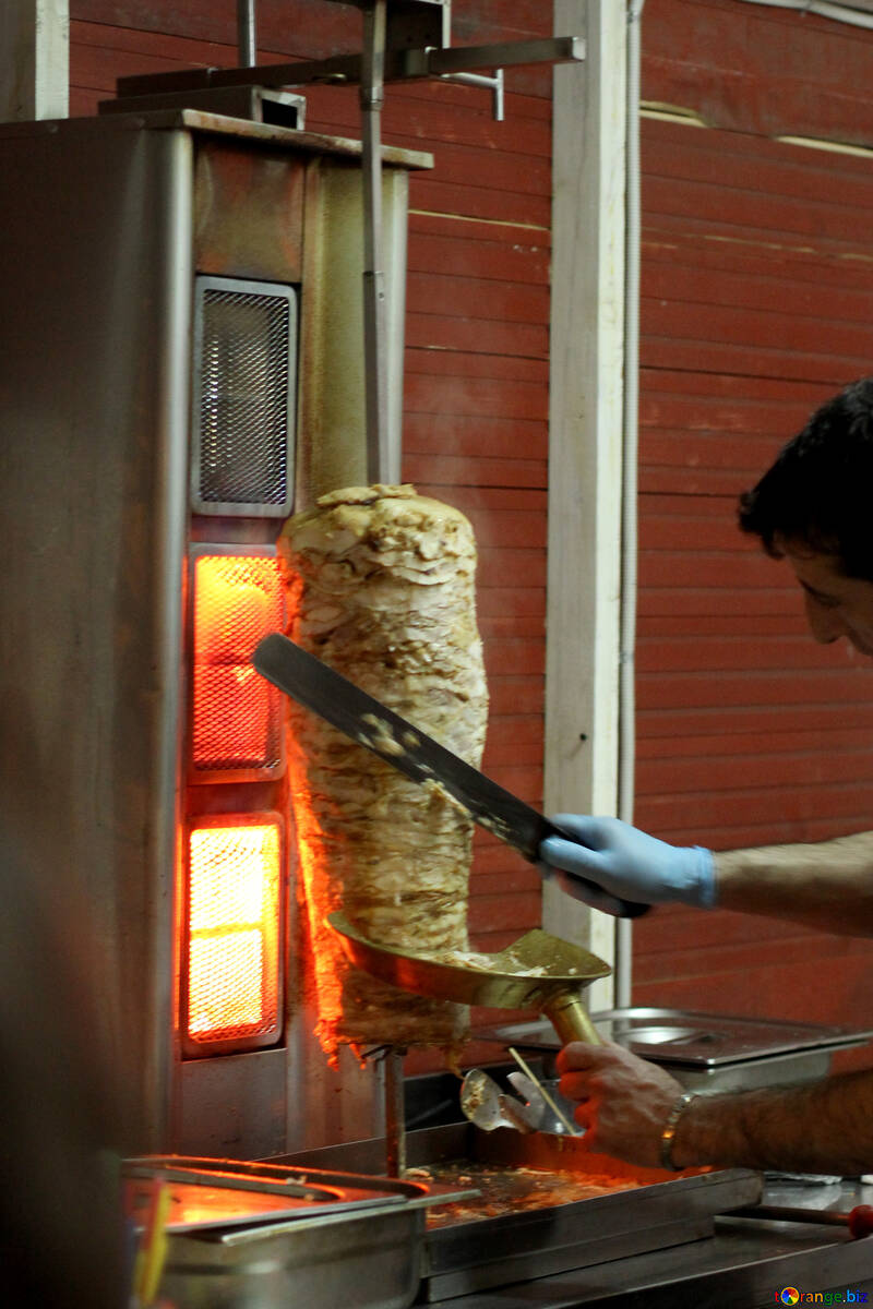 Eine Hand, die Fleisch von einem Stock abschneidet, während Fleisch Schwarma Barbecue-Kebab kocht №53553